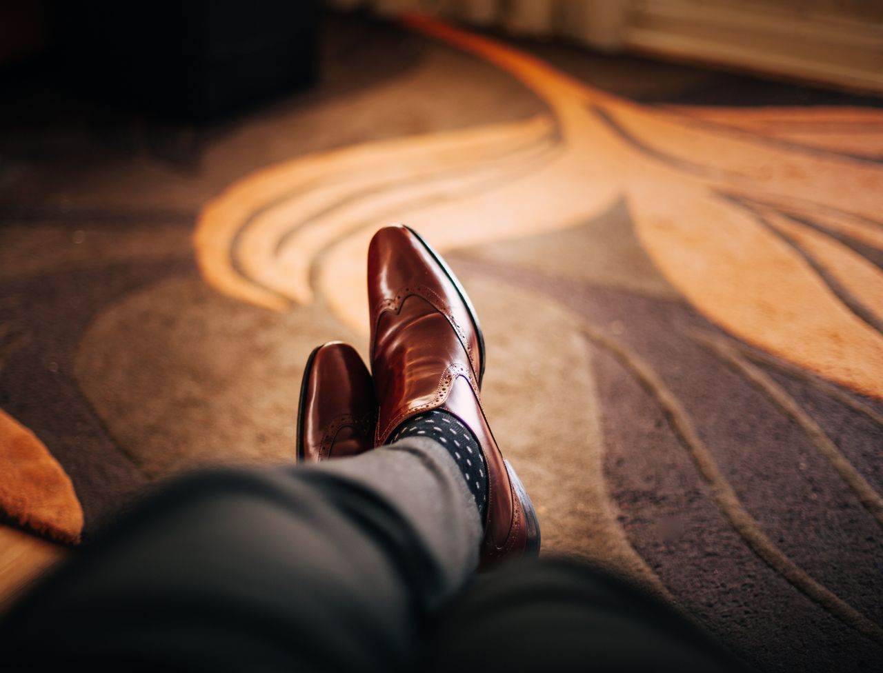 services-04 Close-up of polished brown leather shoes worn with patterned socks, relaxed indoors.