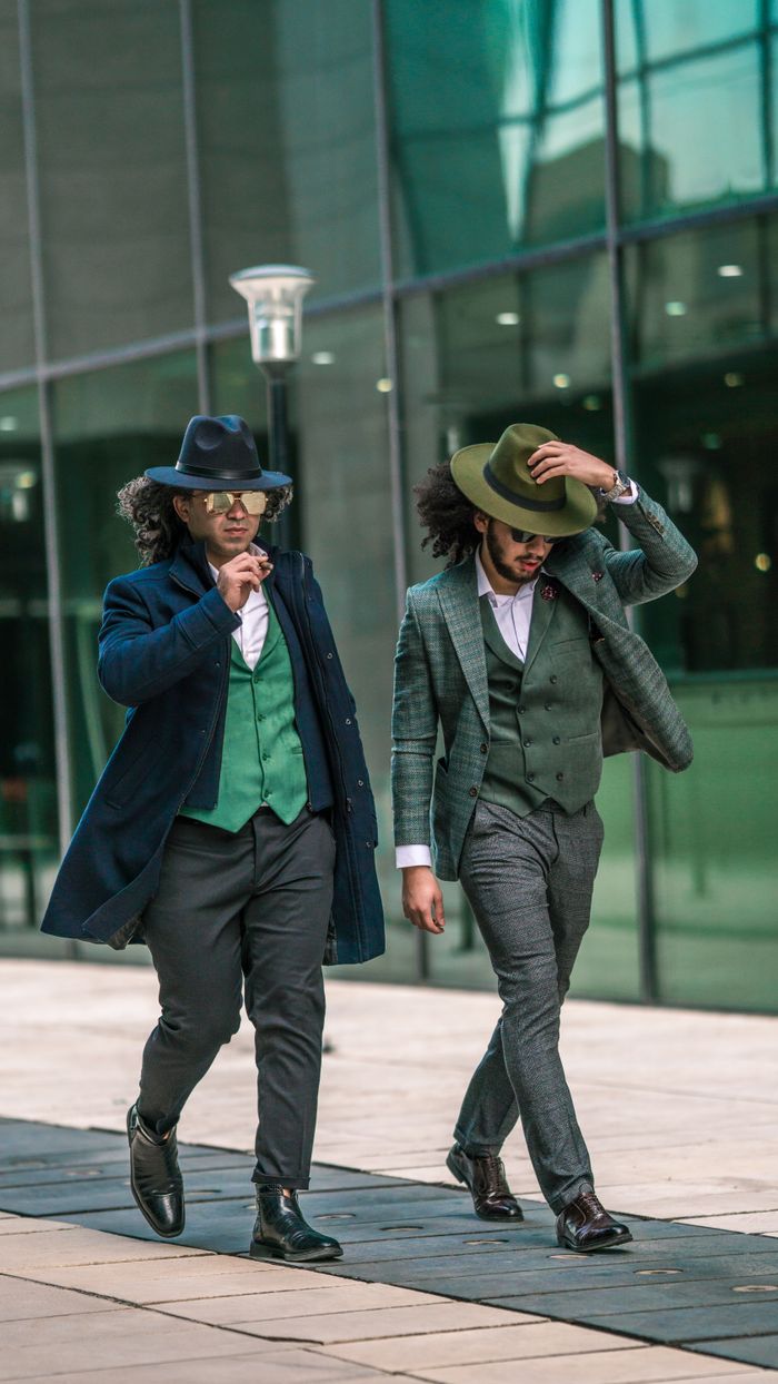 services-03 Two fashionable men in stylish suits and hats confidently walking in an urban setting.