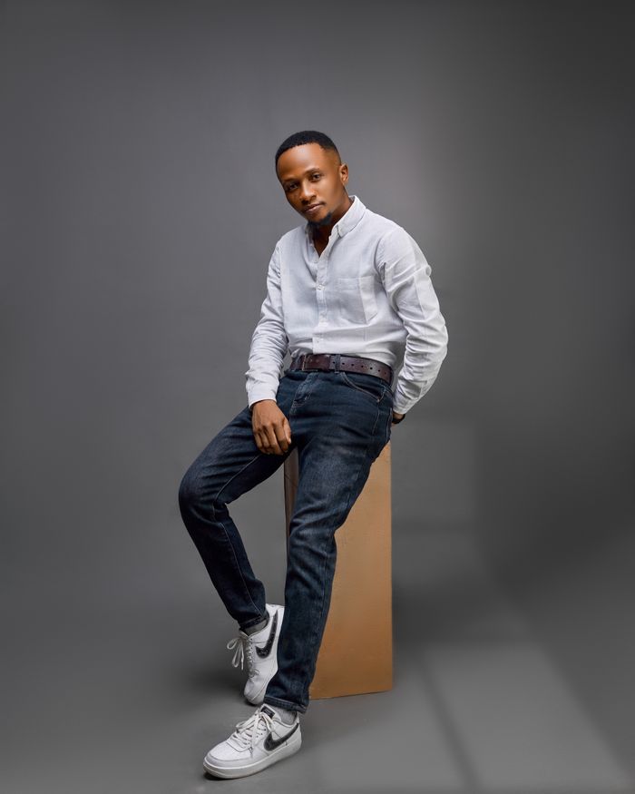services-02 Fashionable male model posing in a studio wearing a white shirt, jeans, and sneakers against a gray background.