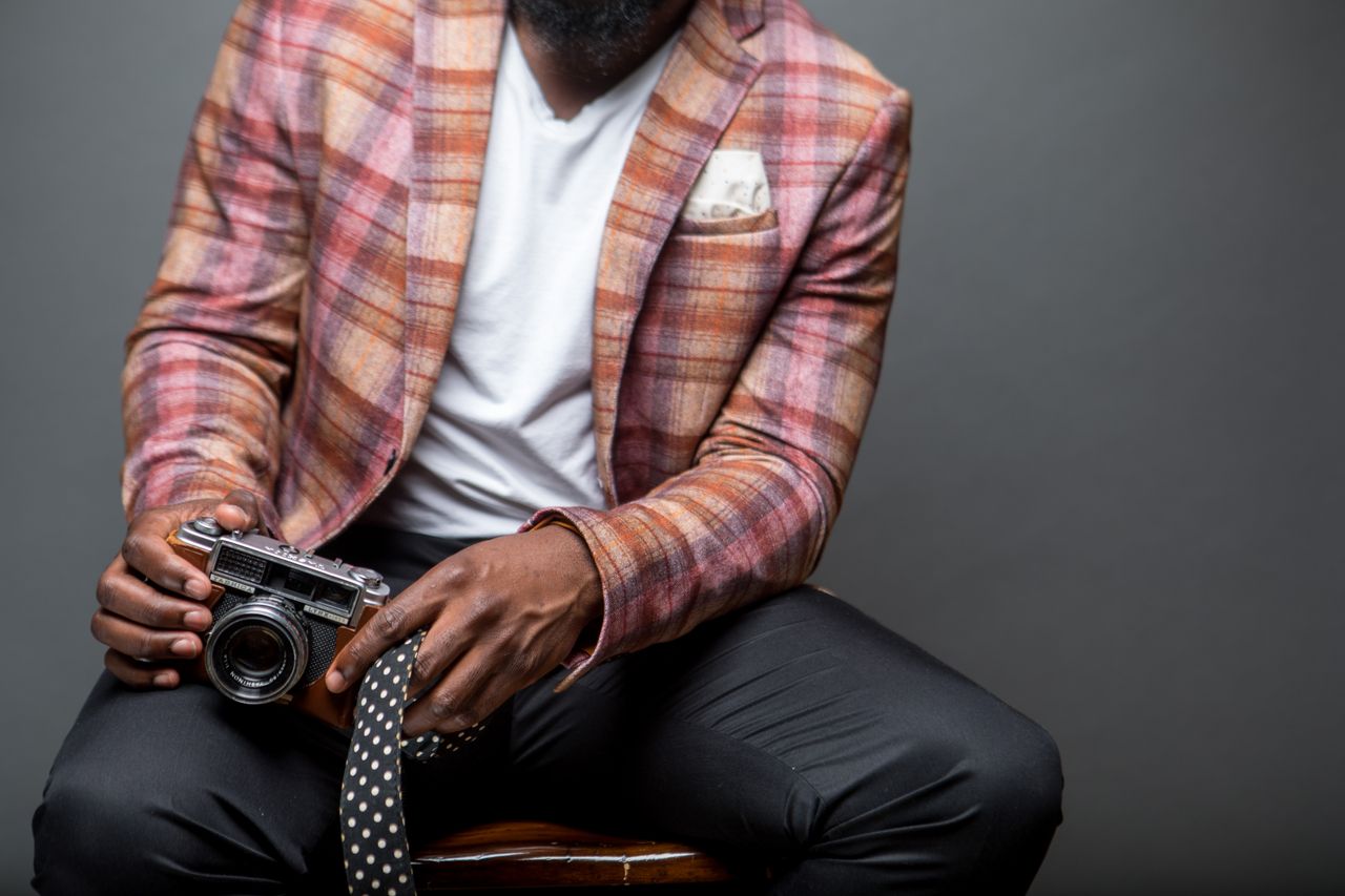 Crafting Captivating Headlines: Your awesome post title goes here A fashionable man in a plaid blazer holds a vintage camera, seated indoors.